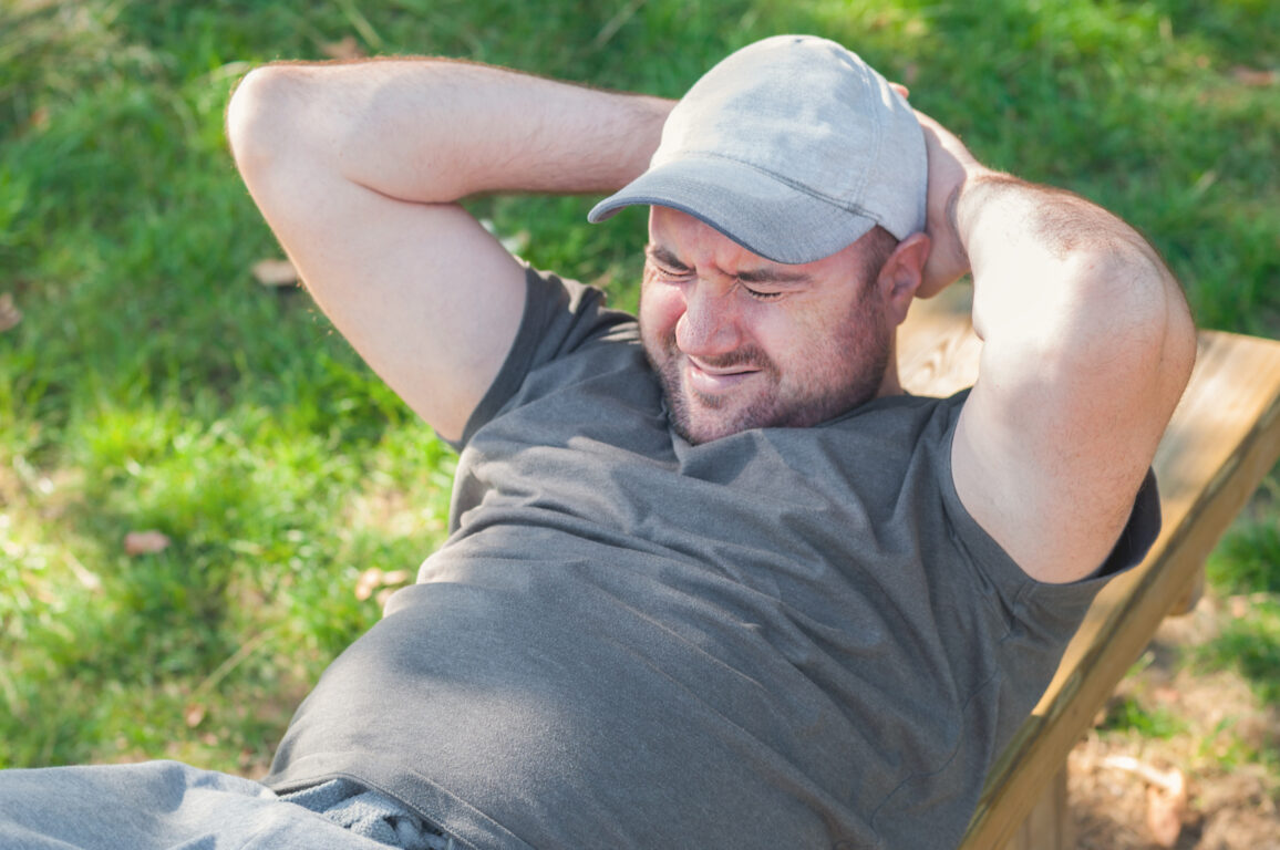 Young man with excess weight doing exercises and rocking his press in the park